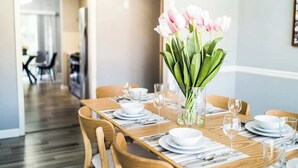 Une table à manger dressée avec de l’assiette blanche, des verres et des couverts, et un vase de tulipes roses placé au centre.