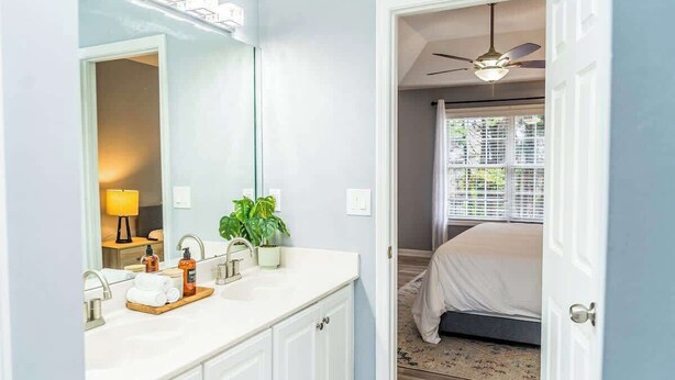 Une salle de bain avec un meuble-lavabo blanc, un grand miroir et un ventilateur de plafond.