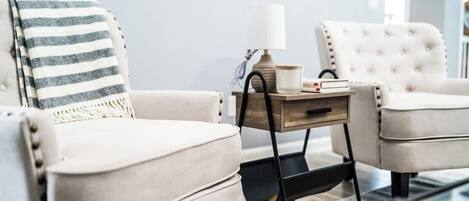 Un salon moderne avec un canapé beige, un plaid rayé, une table d’appoint avec une lampe et un fauteuil blanc.