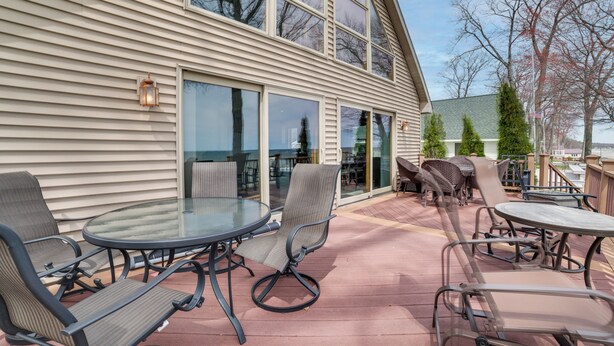An outdoor patio with a glass table and chairs, a sliding glass door, and a view of the sky and trees. - Waterfront Lake Huron Home - Private Beach! (Tawas City)