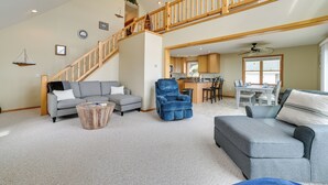 A spacious living area with a high ceiling, a wooden staircase, and a kitchen in the background. - Waterfront Lake Huron Home - Private Beach! (Tawas City)