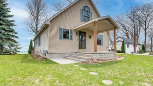 A two-story house with a covered porch, a front yard, and a view of the lake. - Waterfront Lake Huron Home - Private Beach! (Tawas City)