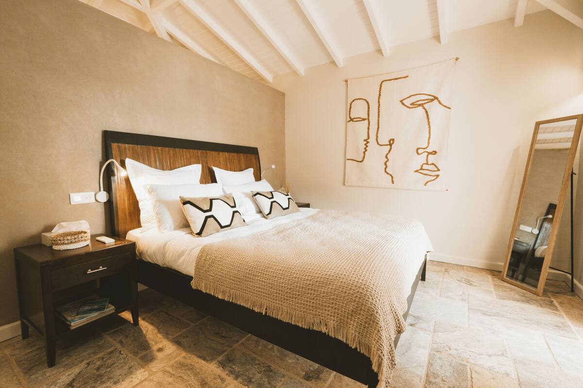 A bedroom with a bed, nightstand, and a wall with a simple line drawing.