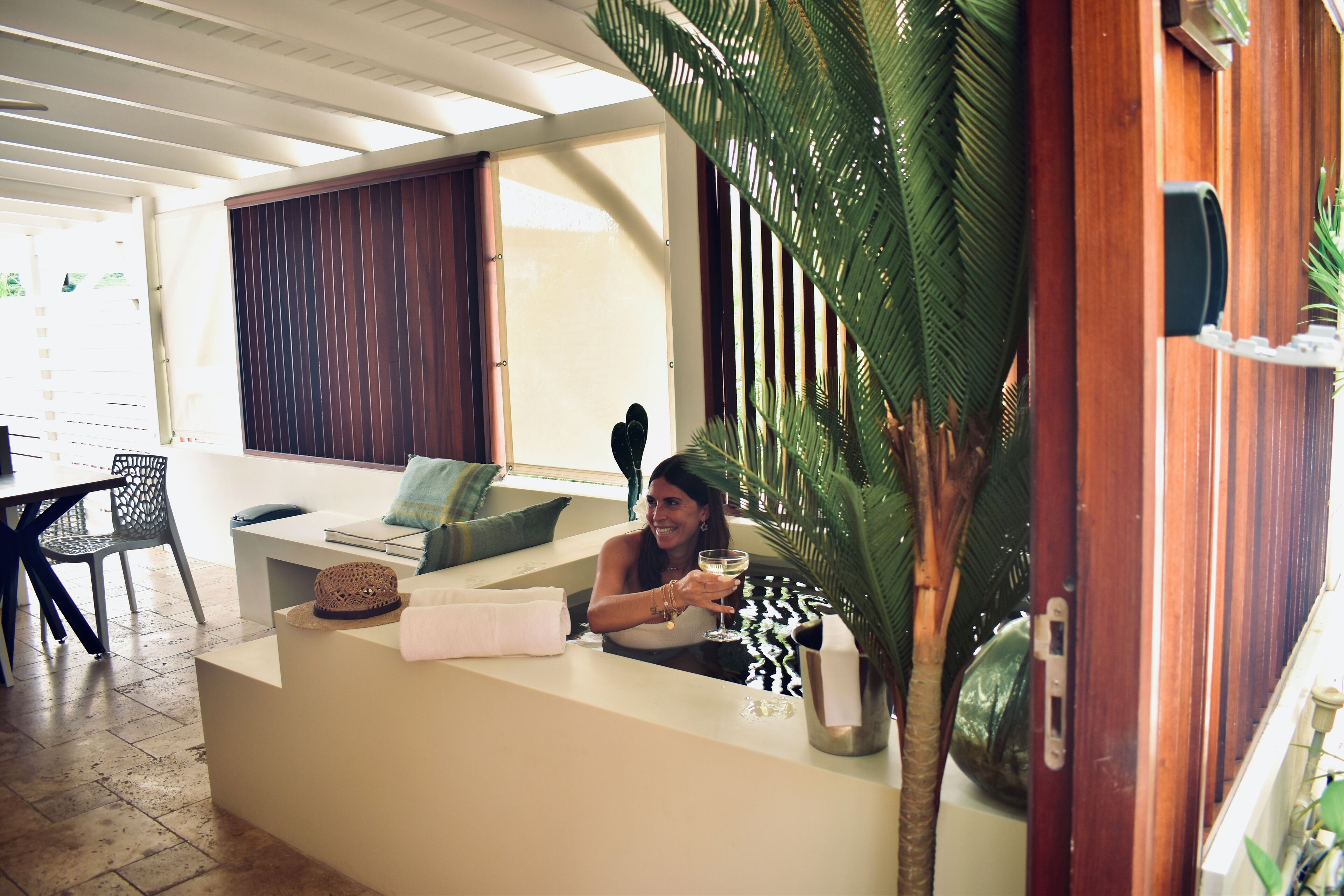 Habitación con mostrador de recepción, sofá, mesa de comedor y sillas. Hay una planta grande y una ventana con cortinas.
