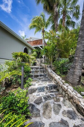 A stone staircase leading to a building with a white exterior and a wooden deck. - La Villa Hibiscus (Orient Bay)