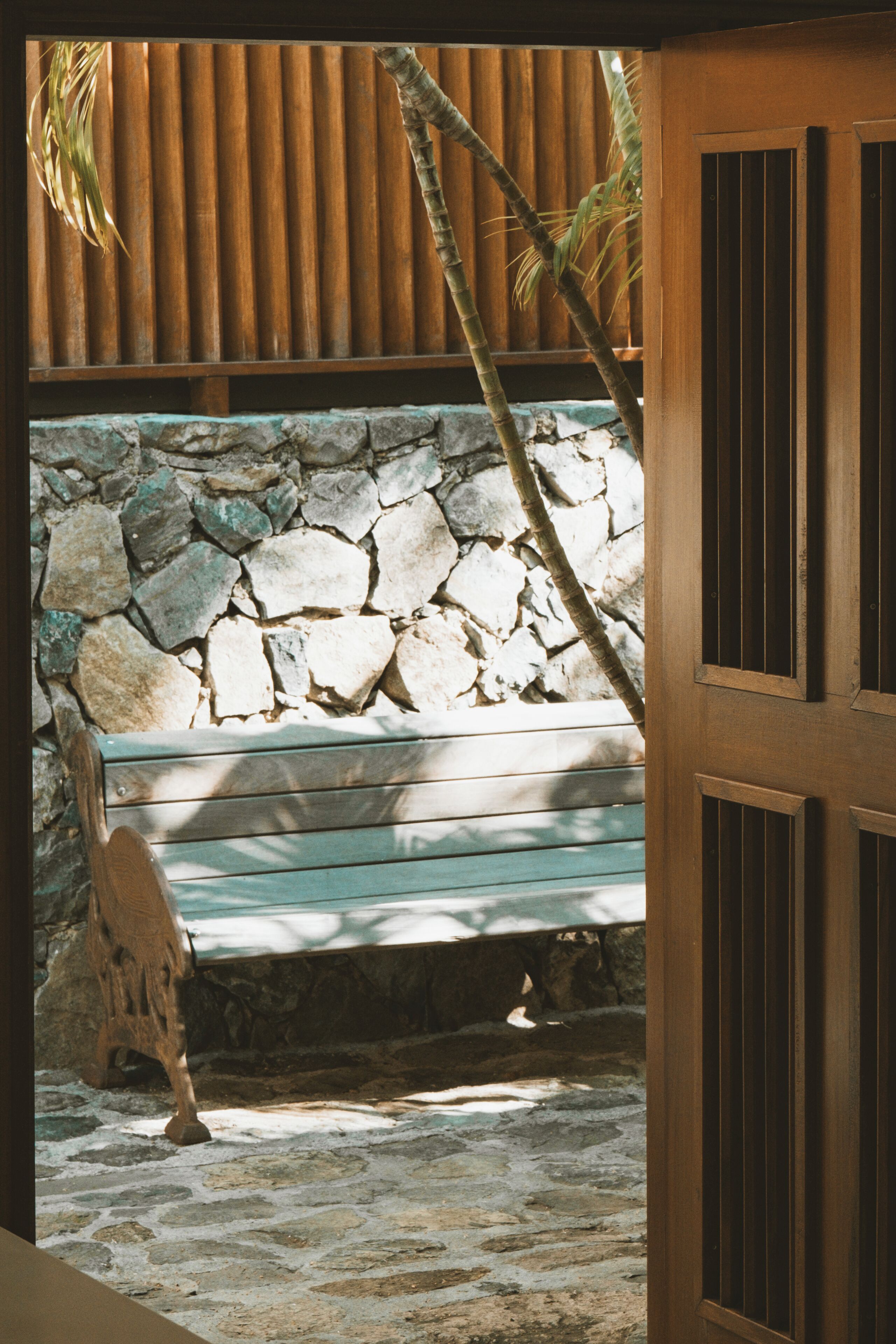 A stone wall, wooden bench, and a door with vertical slats.