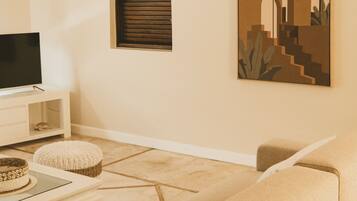 A living room with a beige sofa, a white entertainment unit, a woven hanging light fixture, and a wall-mounted air conditioner.