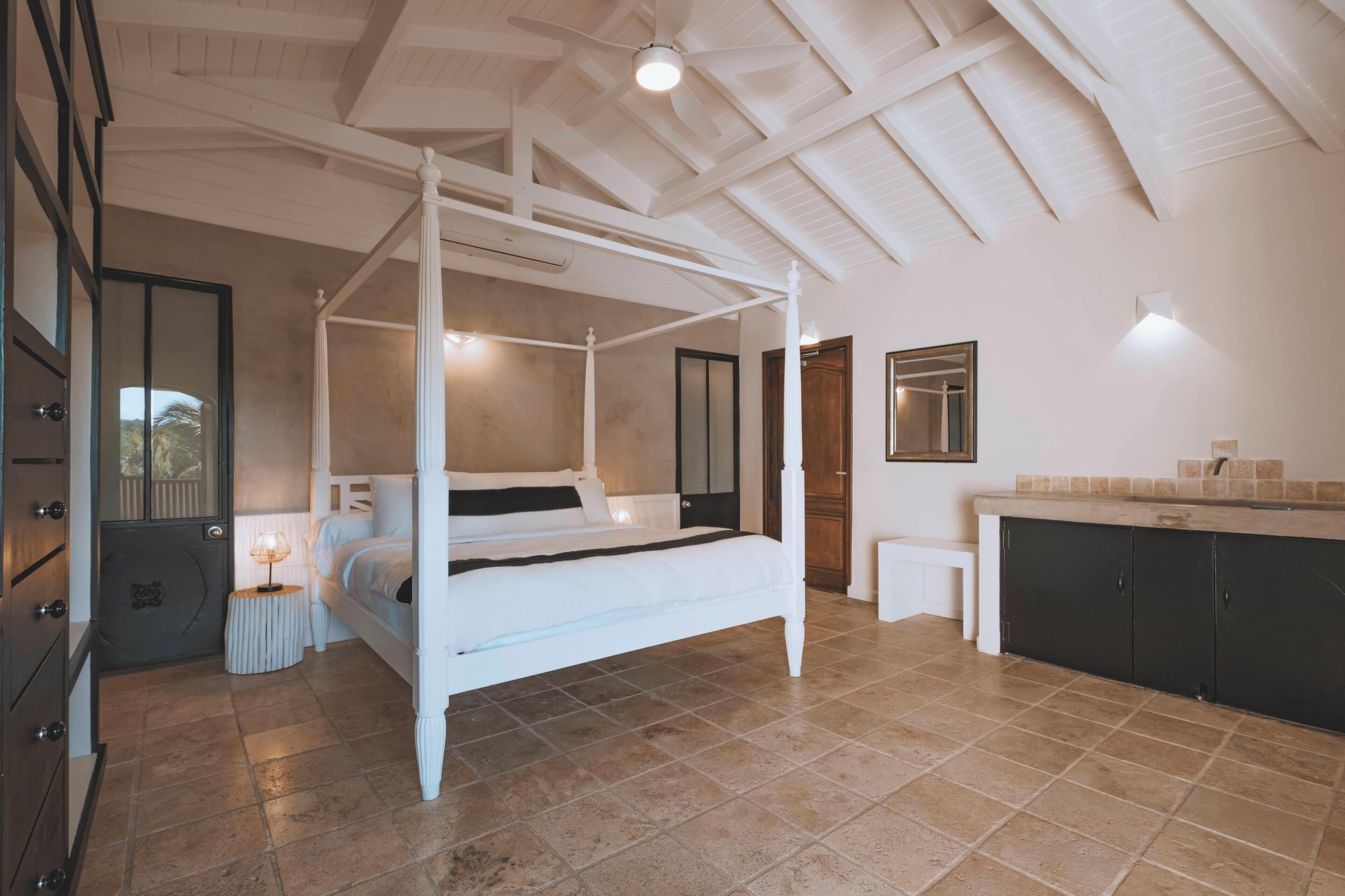 A bedroom with a four-poster bed, a nightstand, a dresser, and a vanity with a mirror.