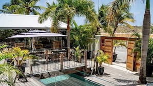Una terraza de madera con piscina, mobiliario exterior y palmeras.