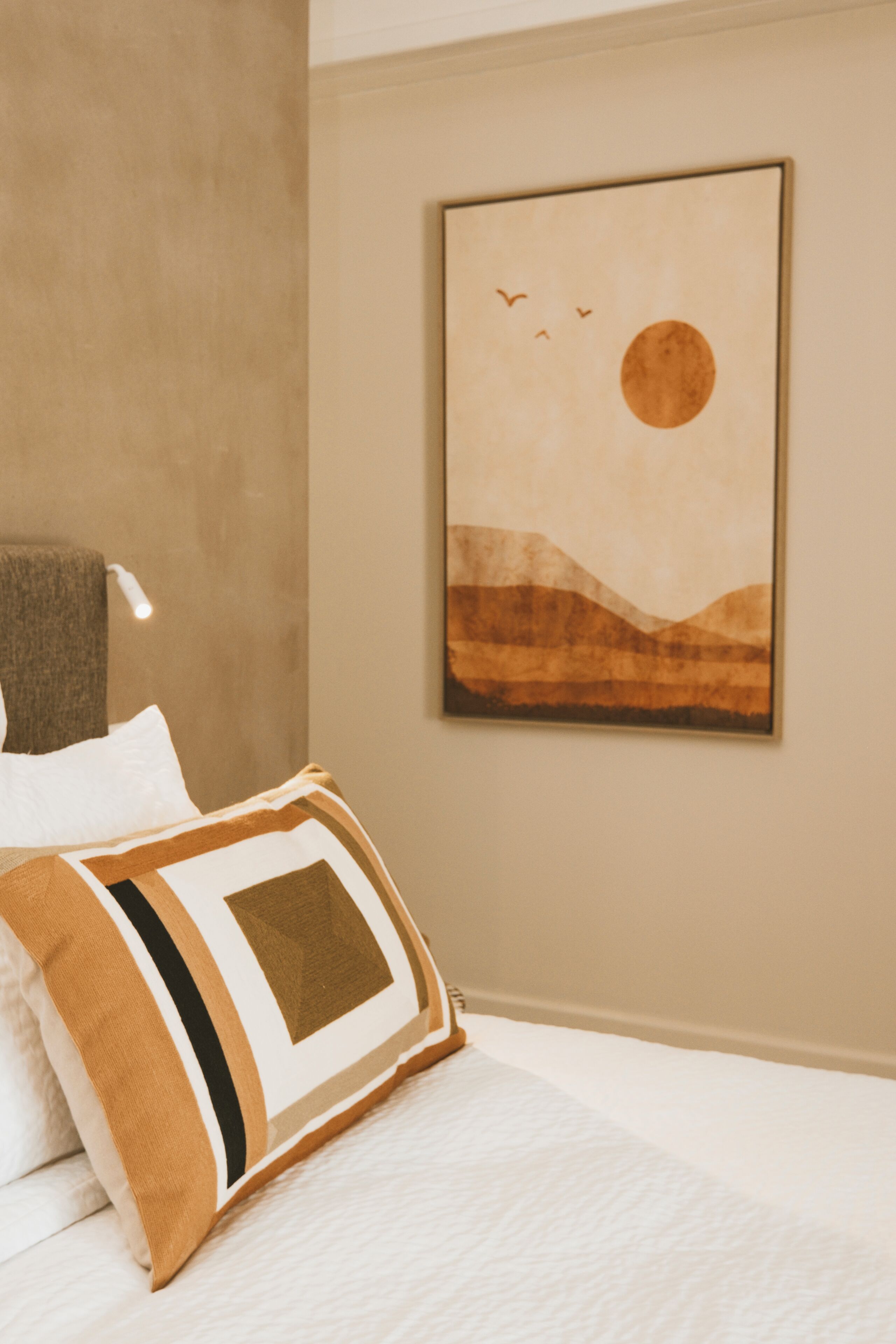 Un dormitorio con cama, almohadas, una obra de arte colgada en la pared y una pared con textura.