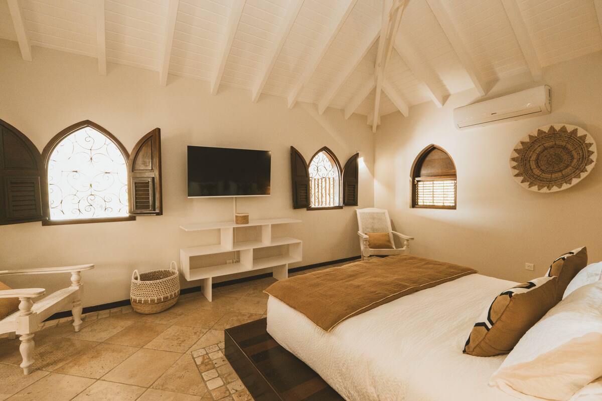 A bedroom with a large bed, a TV, a chair, and a small table.