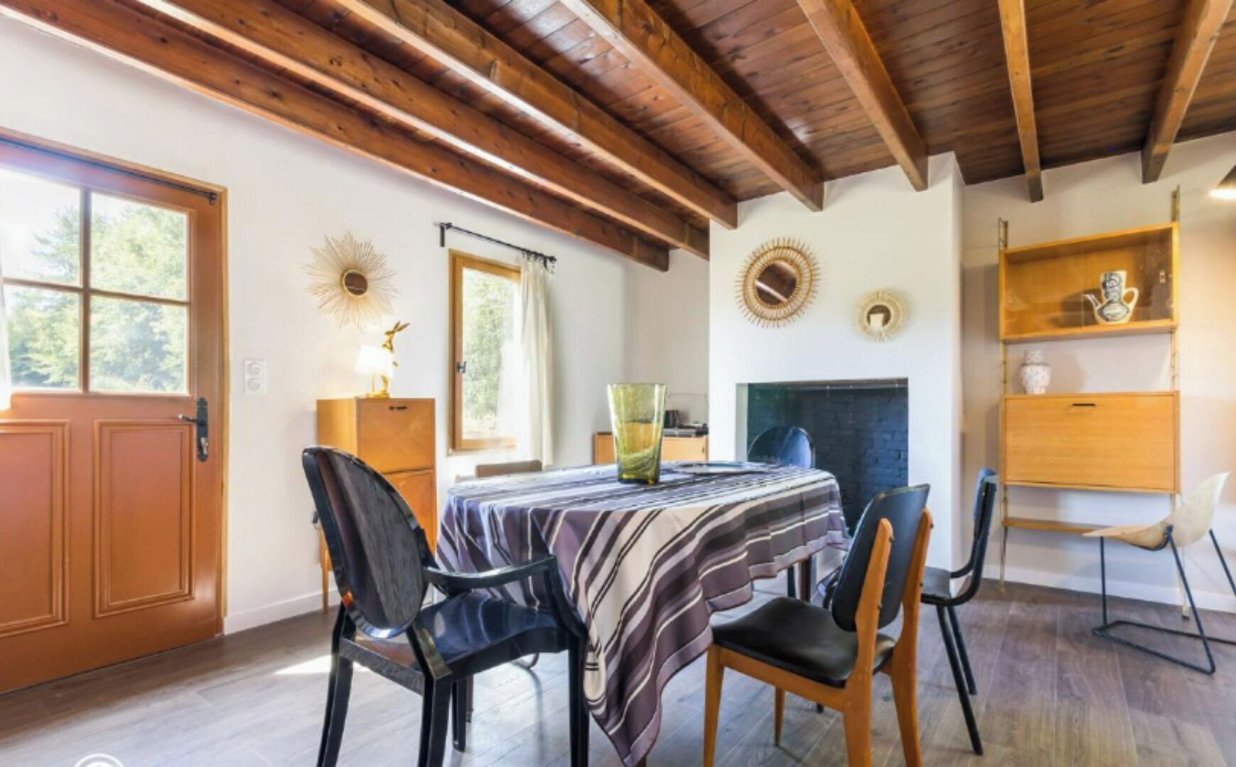 Un coin repas avec une table dressée pour quatre personnes, des chaises en bois, une cheminée et un plafond en bois.