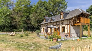 A traditional half-timbered house with a balcony, surrounded by a fenced yard with grass and trees.