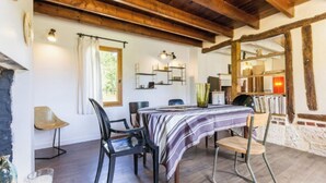 A dining area with a table set for four, wooden beams on the ceiling, and a brick fireplace in the background.