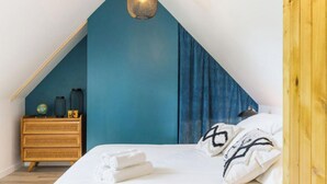 A bedroom with a sloped ceiling, a wooden dresser, a bed with white linens, and a blue accent wall.