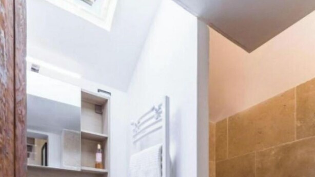 Une salle de bain avec un meuble-lavabo blanc, un porte-serviettes et un espace douche aux carreaux beiges.
