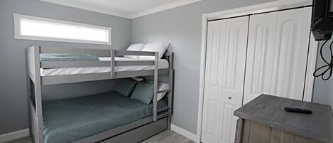 Una cama individual superpuesta con escritorio y televisor en una habitación con paredes grises y una ventana.