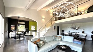 Amplia sala de estar con un sofá seccional de colores claros, una mesa de centro negra y una escalera que conduce a un nivel superior.