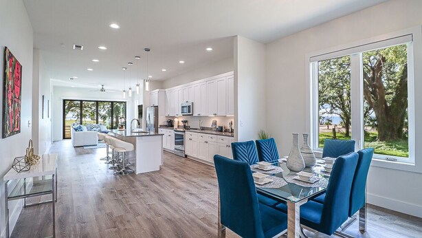 A spacious kitchen with white cabinets, a central island, and a dining area with blue chairs.