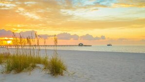 A beach scene with a pier extending into the water, a boat, and a small structure on the pier.