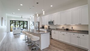 A modern kitchen with white cabinets, a central island with bar stools, stainless steel appliances, and pendant lighting.