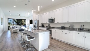 Una cocina moderna con armarios blancos, electrodomésticos de acero inoxidable y una zona de bar con taburetes.