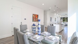 Un comedor moderno con una mesa de vidrio, sillas tapizadas en gris y jarrones decorativos.
