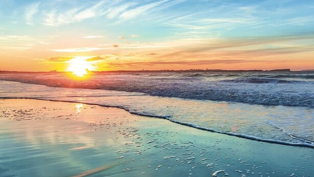 Escena de playa con el sol poniéndose sobre el océano, olas acariciando suavemente la orilla.