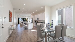 Una cocina moderna con armarios blancos, una isla central y un comedor con mesa y sillas de vidrio.