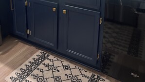 Una cocina con armarios azul oscuro, encimera de granito, lavavajillas integrado y una ventana con persianas.