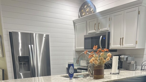 Una cocina con refrigerador de acero inoxidable, microondas, dispensador de agua, lavamanos y una zona con taburetes de bar.