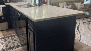 Una cocina con una isla grande, muebles oscuros, una cafetera y un florero con flores.