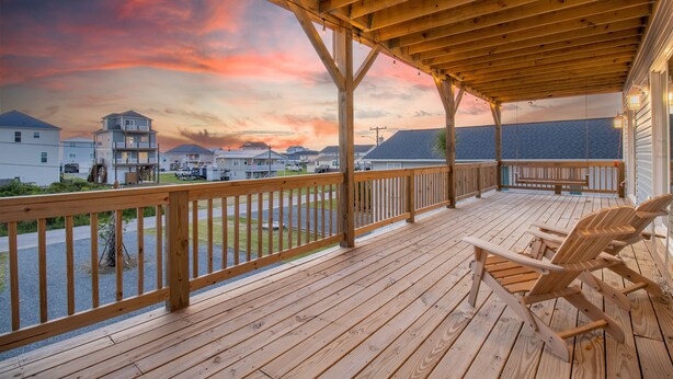 Een houten terras met uitzicht op huizen en een zonsondergang.