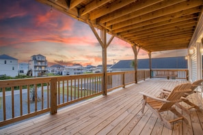 Una terraza de madera con vistas a casas y un atardecer.