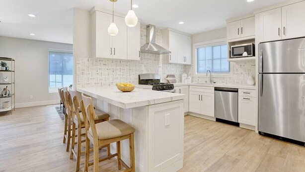 A modern kitchen with white cabinetry, a central island with bar stools, stainless steel appliances, and pendant lighting. - Upscale Family Home · 5 miles to Disneyland (Fullerton)