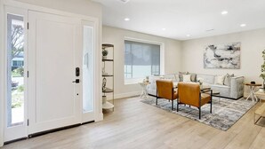 A spacious living room with a large window, a grey sofa, a coffee table, and a dining area with chairs. - Upscale Family Home · 5 miles to Disneyland (Fullerton)