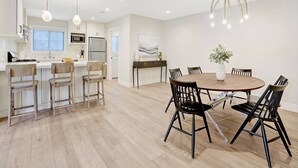 A modern kitchen with white cabinets, a central island with bar stools, and a dining area with a round table and chairs. - Upscale Family Home · 5 miles to Disneyland (Fullerton)