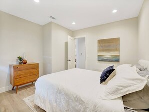 A bedroom with a large bed, a wooden dresser, and a painting on the wall.