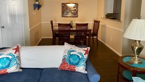 A living room with a blue sofa, a dining area with wooden chairs, a chandelier, and a lamp. - K4 Gulf Shores Vacation Getaway II (Gulf Shores)
