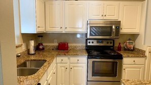 A kitchen with white cabinets, a stainless steel stove, a microwave, and granite countertops. - K4 Gulf Shores Vacation Getaway II (Gulf Shores)