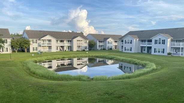 A residential complex with multiple two-story buildings, a central pond reflecting the structures, and a well-maintained lawn. - K4 Gulf Shores Vacation Getaway II (Gulf Shores)