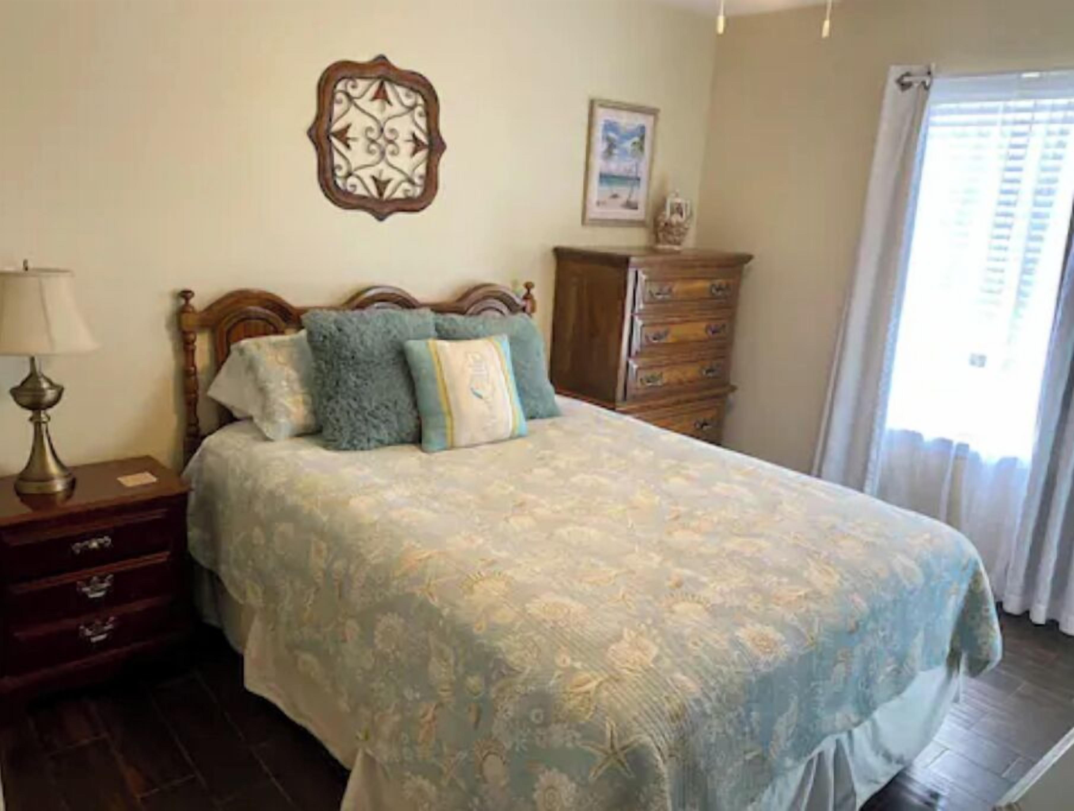 Makuuhuone, jossa on sänky, lipasto, yöpöytä, lamppu, koristeellinen seinäelementti ja ikkuna, jossa on verhot.