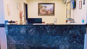 Un mostrador de recepción con encimera de mármol, un cuadro de paisaje enmarcado en la pared y un reloj encima.