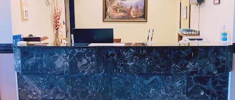 A reception desk with a marble top, a framed landscape painting on the wall, and a clock above it.