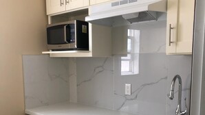 Una cocina con armarios blancos, un lavamanos de acero inoxidable, un microondas y un lavavajillas.