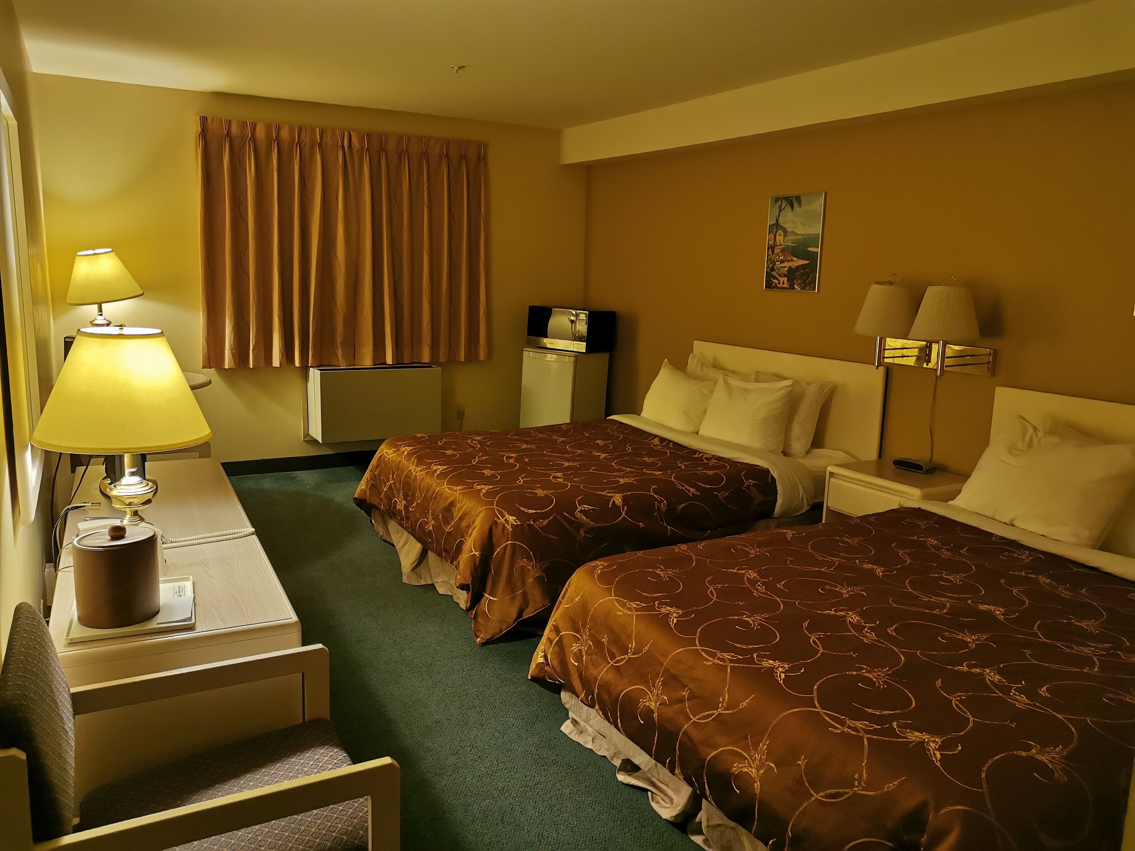 A hotel room with two beds, a desk, a chair, a lamp, a television, and a painting on the wall.