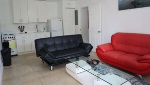 A compact living space with a kitchenette, a black leather sofa, a red sofa, and a glass coffee table.