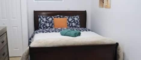 Un dormitori amb llit, ventilador al sostre, finestra amb persianes i una porta.