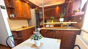 Eine moderne Küche mit Holzschränken, einem Edelstahlkühlschrank und einem Essbereich mit Tisch und Stühlen.