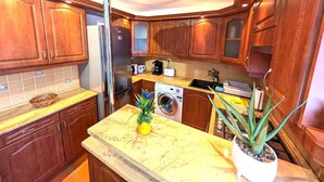 Eine Küche mit Holzschränken, einem Edelstahl-Kühlschrank, einer Waschmaschine und einem Spülbecken.